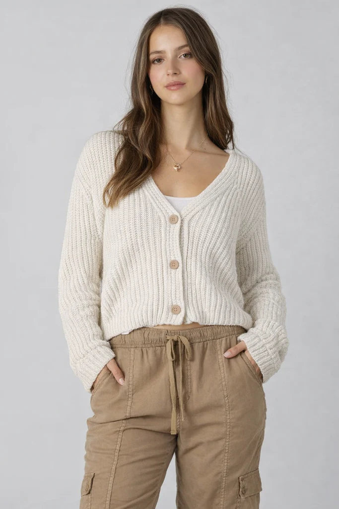Woman wearing a cream knitted cardigan and beige cargo pants on a gray background