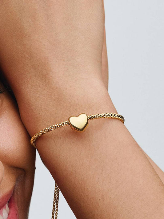 Gold bracelet with a heart charm on a wrist against a neutral background