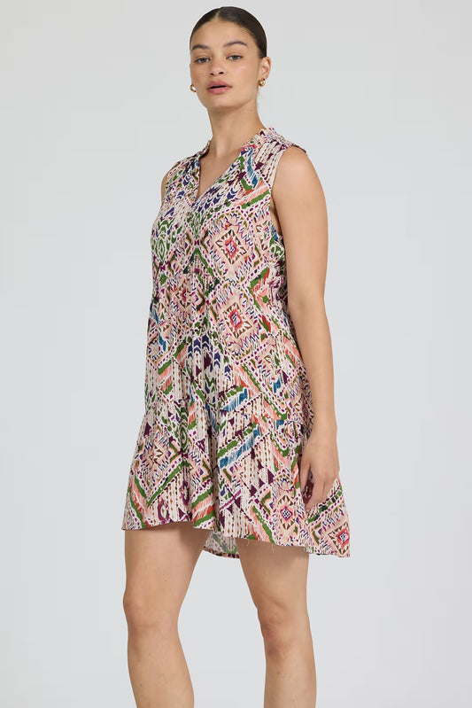 Woman wearing a sleeveless, patterned dress on a plain background