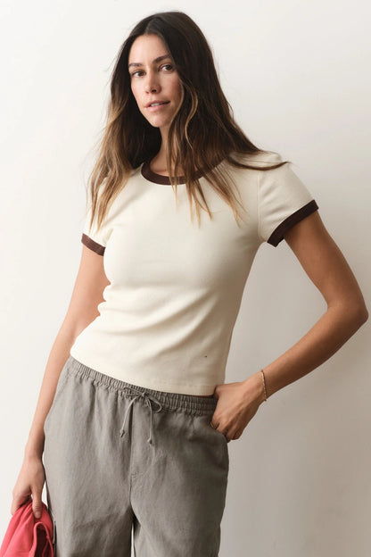 Woman wearing a white t-shirt with black trim and gray pants against a plain background