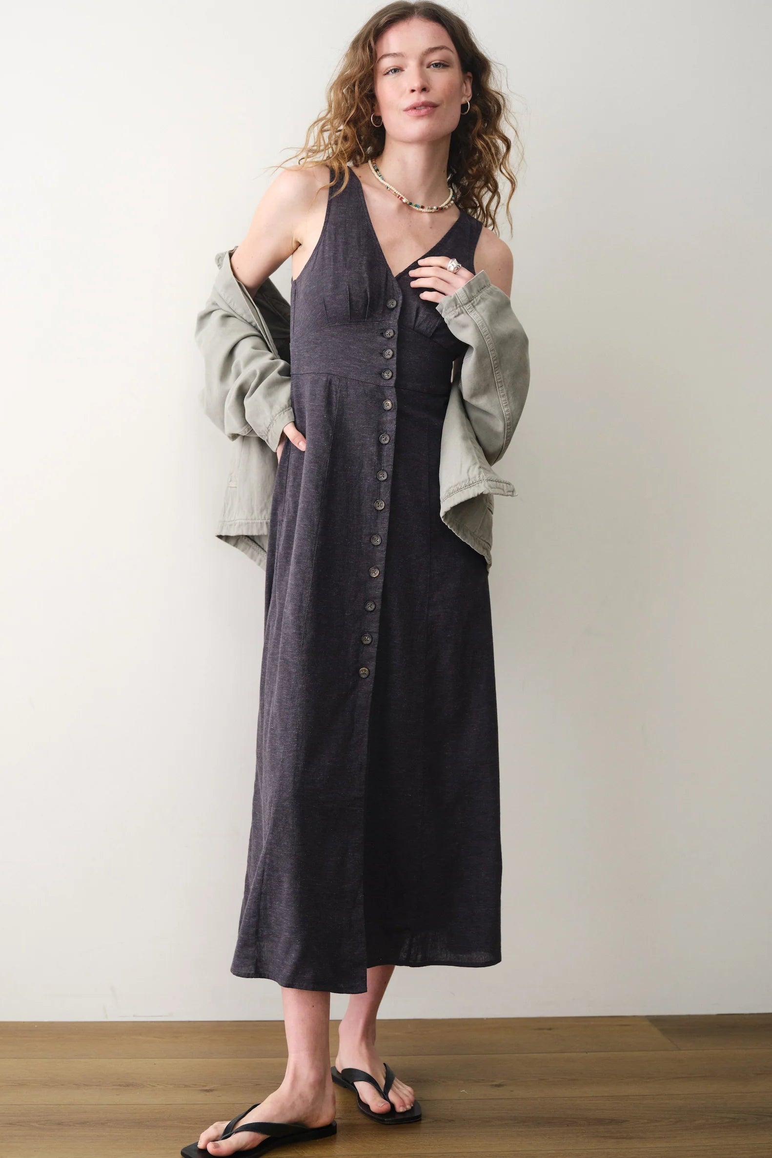 Woman wearing a black dress with a light gray cardigan against a white wall.