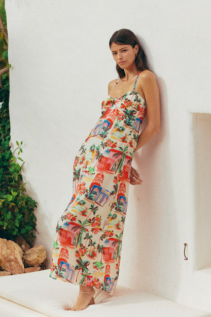Woman wearing a colorful floral dress against a white wall with greenery.