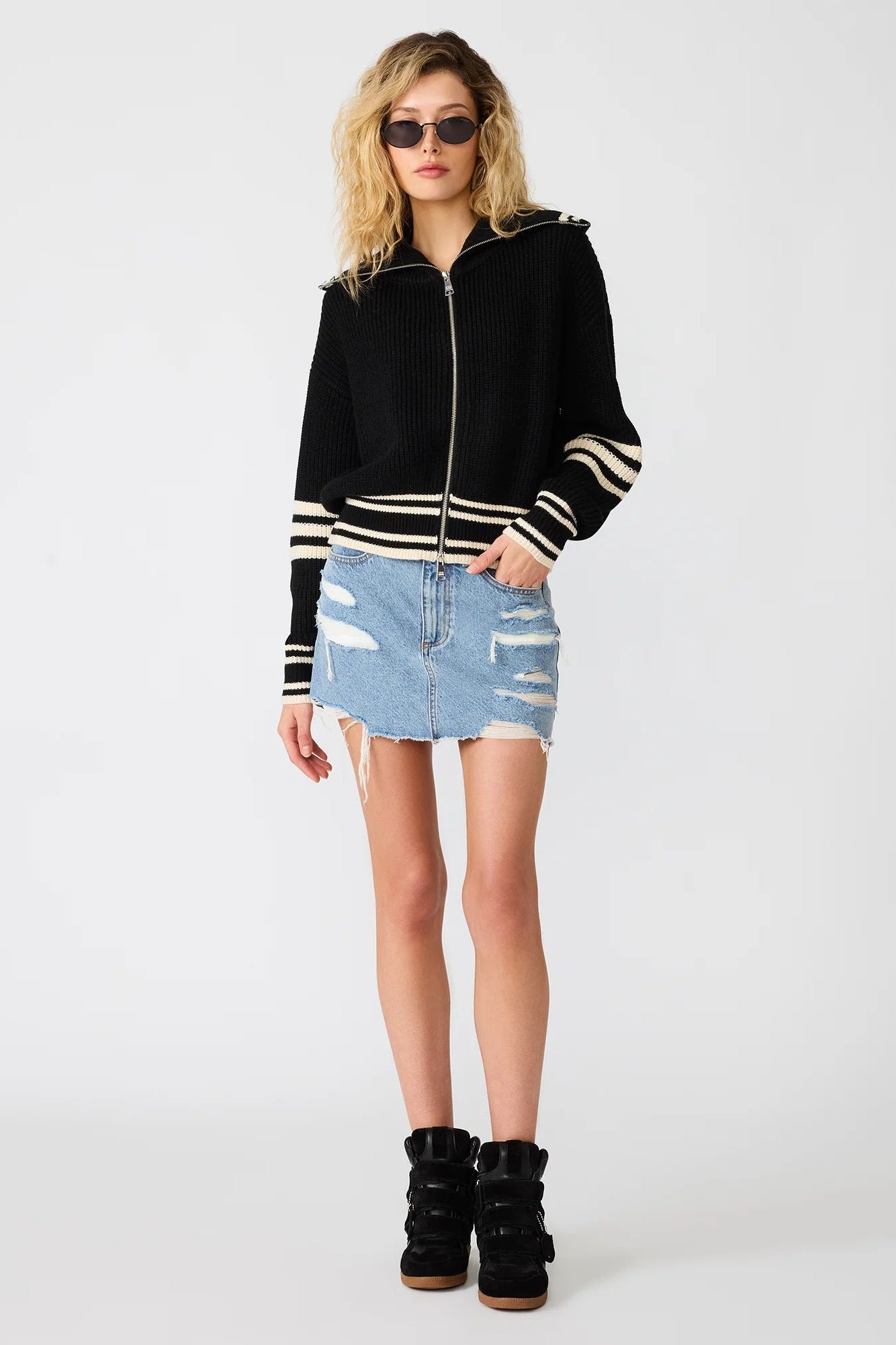 Woman wearing a black hoodie with white stripes, denim skirt, and black boots on a white background