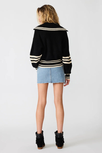 Person wearing a black and white striped sweater with a denim skirt on a white background