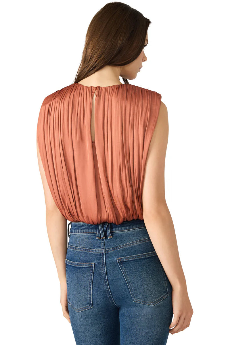 Woman wearing a rust-colored sleeveless top and blue jeans on a white background