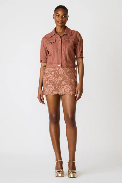 Woman wearing a pink denim jacket and lace skirt on a white background