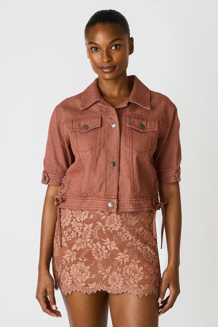 Woman wearing a brown denim jacket over a lace dress on a white background