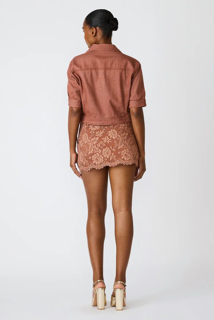Person wearing a brown denim shirt and lace skirt on a white background