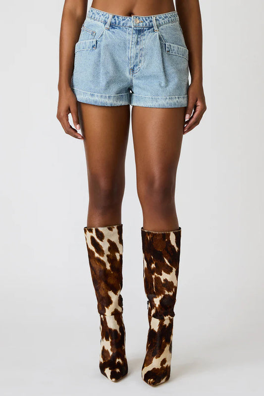 Person wearing cow print knee-high boots with denim shorts on a white background