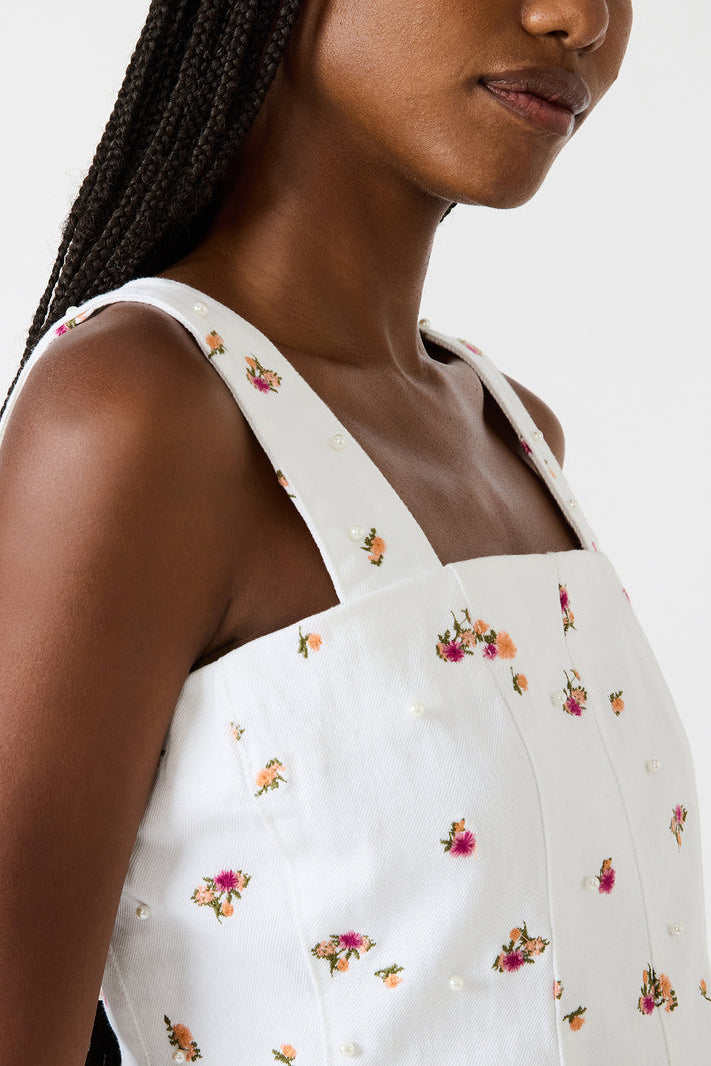 Woman wearing a white dress with floral patterns on a plain background