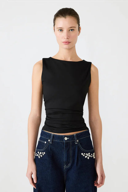 Woman wearing a black sleeveless top and blue jeans with decorative elements on a white background