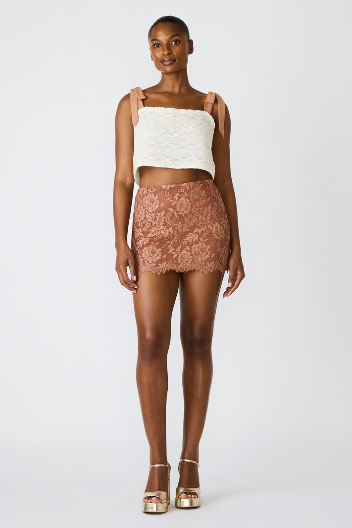 Woman wearing a white lace top and brown lace skirt on a white background