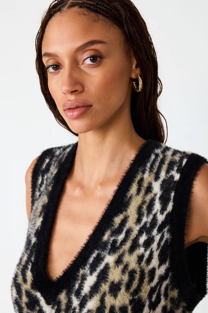 A close-up of a model wearing a fuzzy leopard-print sleeveless vest with black trim, set against a plain light gray background.