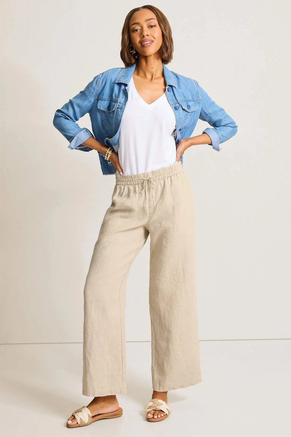 Woman wearing a denim jacket, white top, and beige pants against a light background