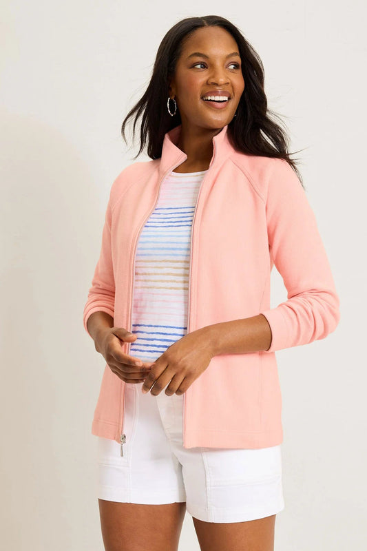 Woman wearing a pink jacket over a striped shirt and white shorts on a plain background