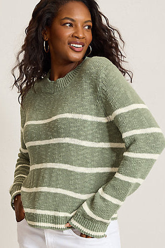A woman wearing a sage green knit sweater with horizontal cream stripes, paired with white pants, photographed against a plain light beige background.