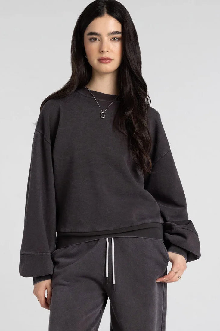 A woman modeling a dark charcoal gray oversized crewneck sweatshirt with matching sweatpants against a light gray studio background.