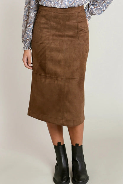 A brown suede-like midi skirt worn by a model, paired with a patterned blouse and black ankle boots, against a plain light gray studio background.