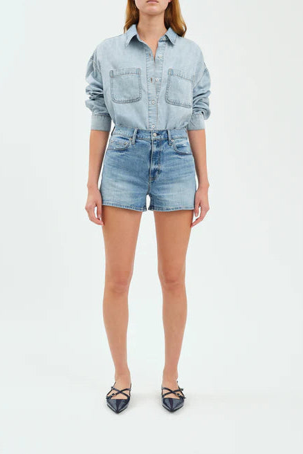 Person wearing a light blue denim shirt and shorts on a white background