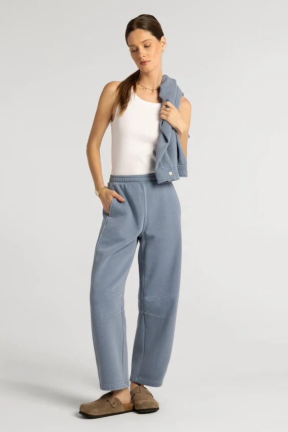Woman wearing light blue pants and a white top on a gray background