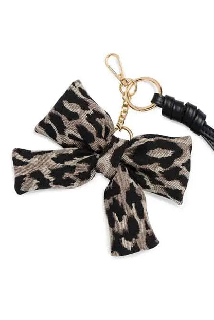 A leopard print fabric bow keychain charm with a black leather tassel and gold-tone metal hardware, shown on a plain white background.