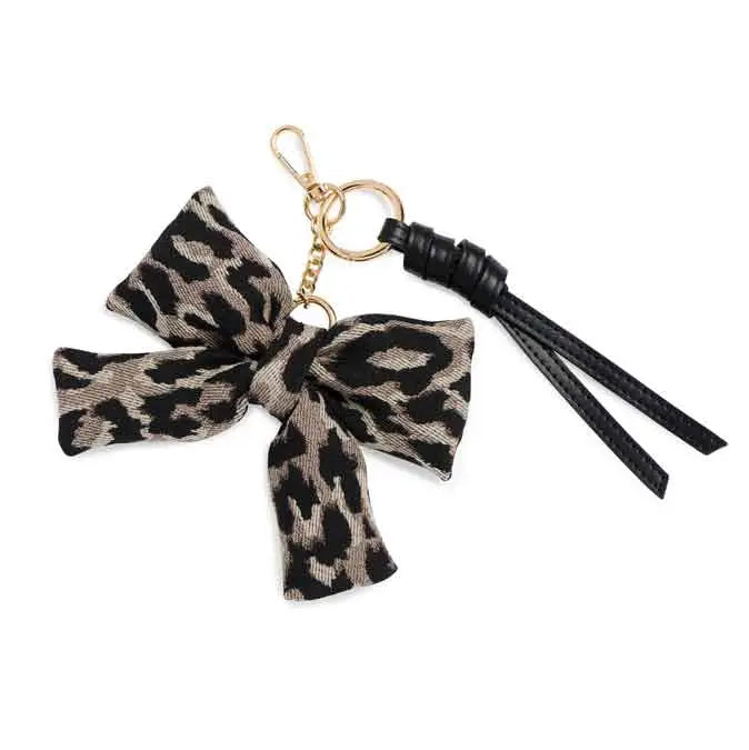 A leopard print fabric bow keychain charm with a black leather tassel and gold-tone metal hardware, shown on a plain white background.