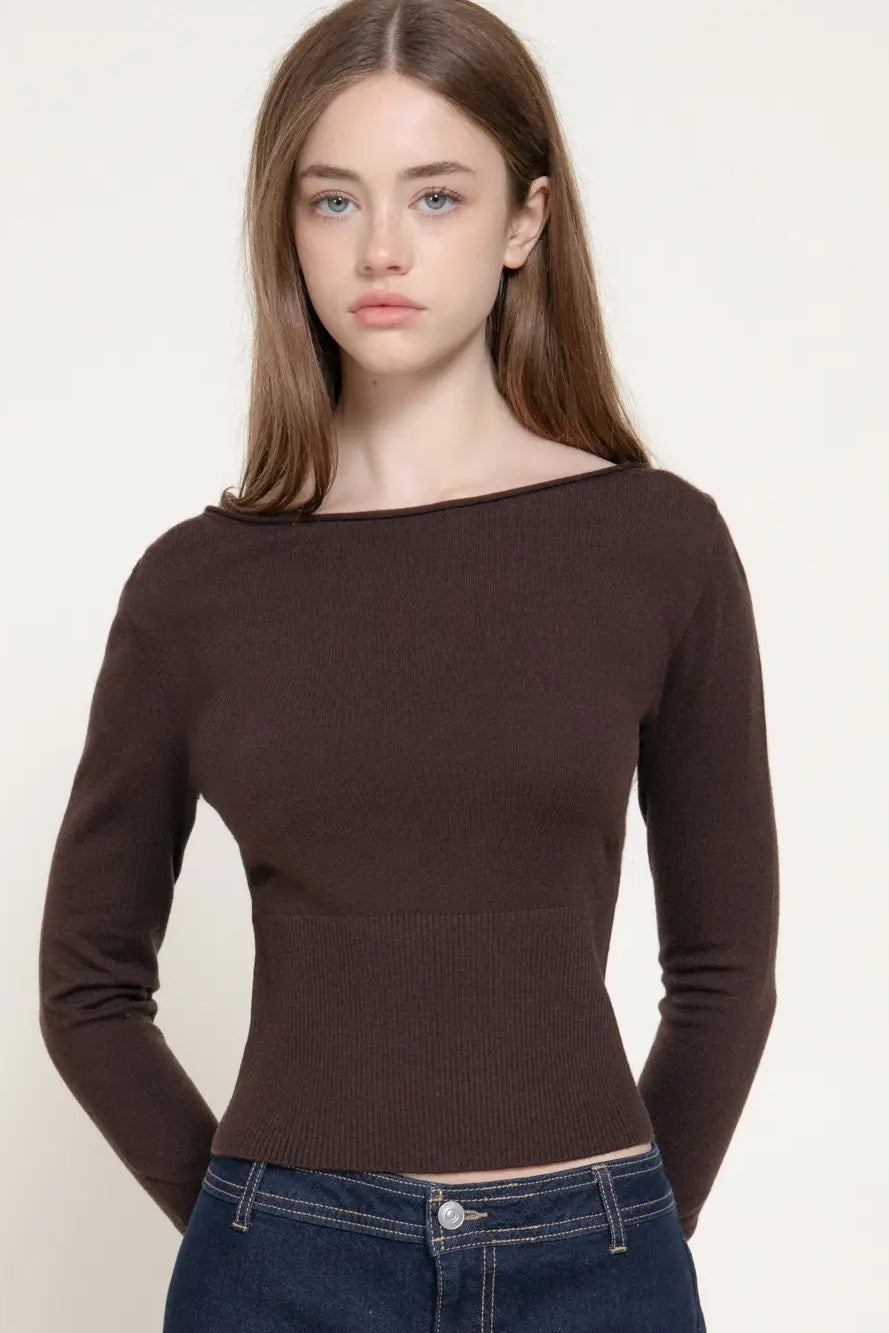 A woman modeling a dark brown ribbed knit long-sleeve top with a wide boat neckline, paired with dark blue jeans, against a plain off-white background.