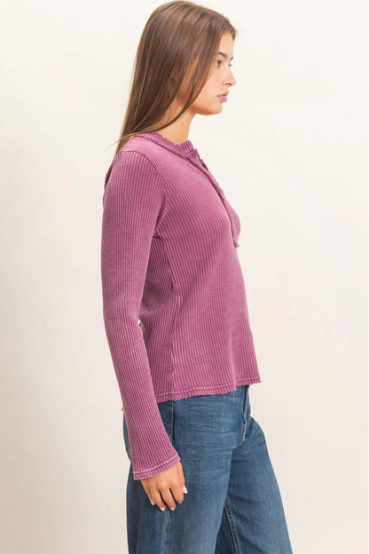 A woman shown in side profile wearing a ribbed long-sleeve henley-style top in dusty mauve-pink with blue jeans, against a plain light beige studio background.
