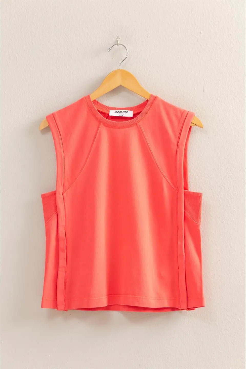 Coral sleeveless top on a wooden hanger against a beige background