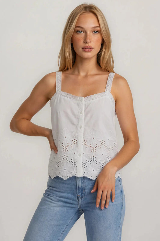Woman wearing a white lace top and blue jeans against a plain background
