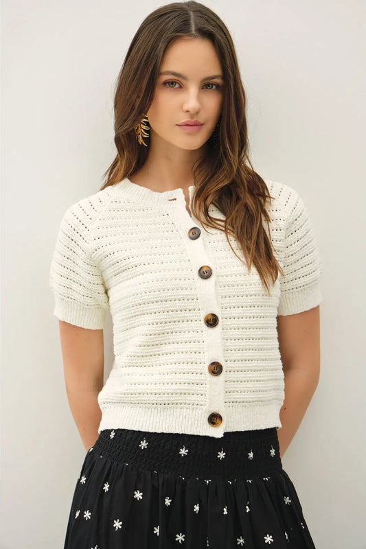 Woman wearing a white textured cardigan with brown buttons against a plain background