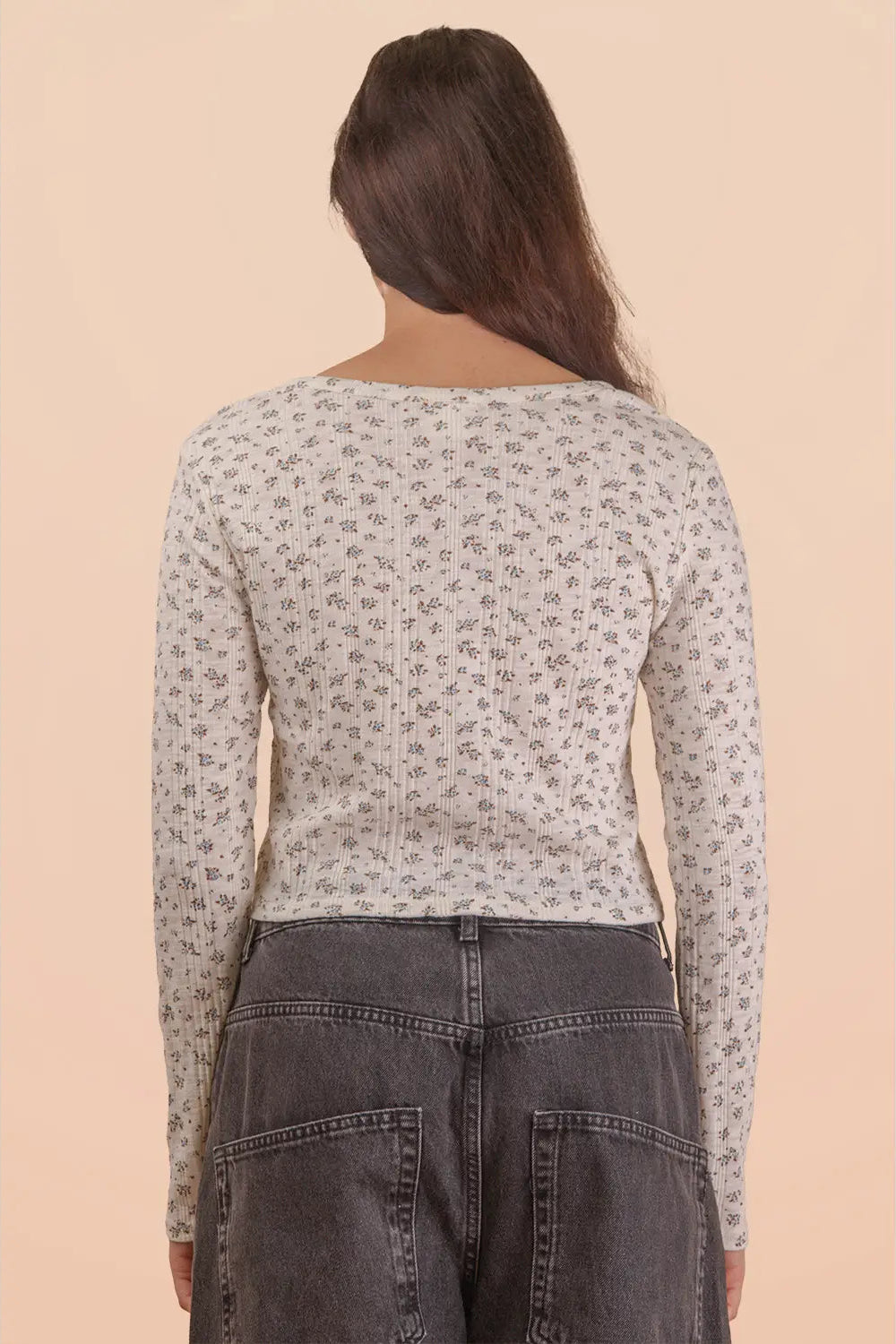 Person wearing a patterned long-sleeve top and dark jeans on a beige background