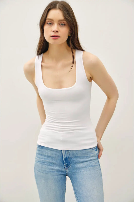 Woman wearing a white tank top and light blue jeans against a plain background