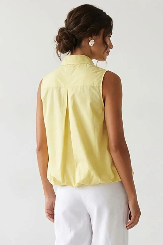 Woman wearing a yellow sleeveless blouse against a white background