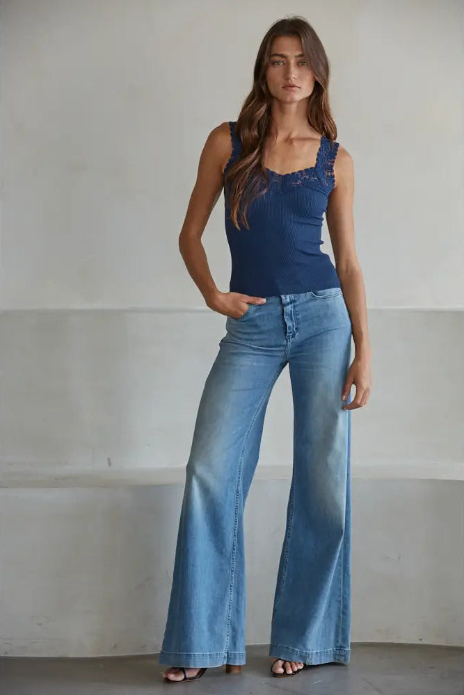 Woman wearing a blue lace top and wide-leg jeans against a plain background