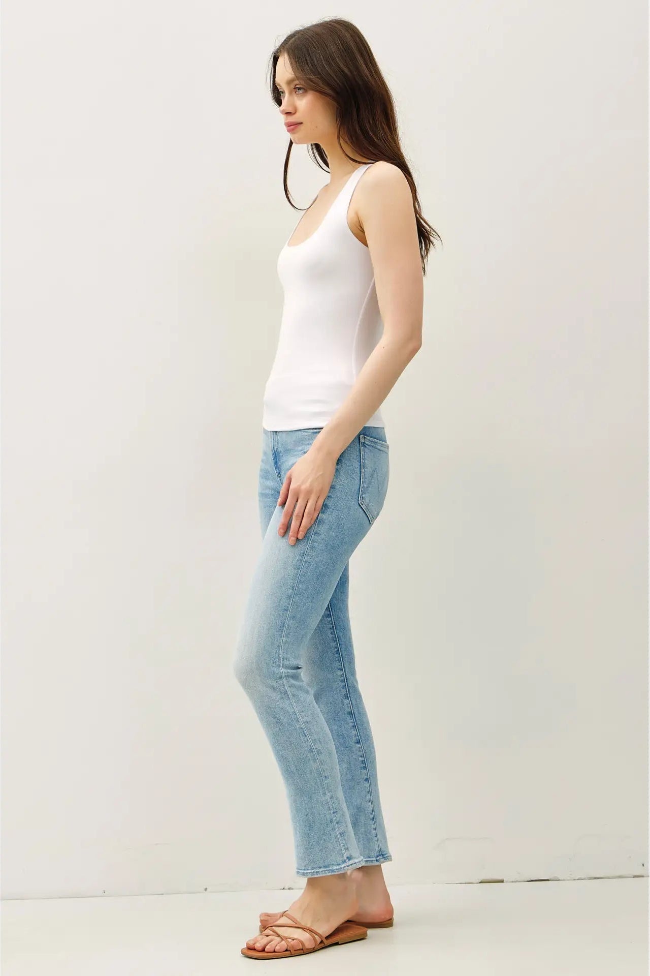 Woman wearing a white tank top and light blue jeans on a white background