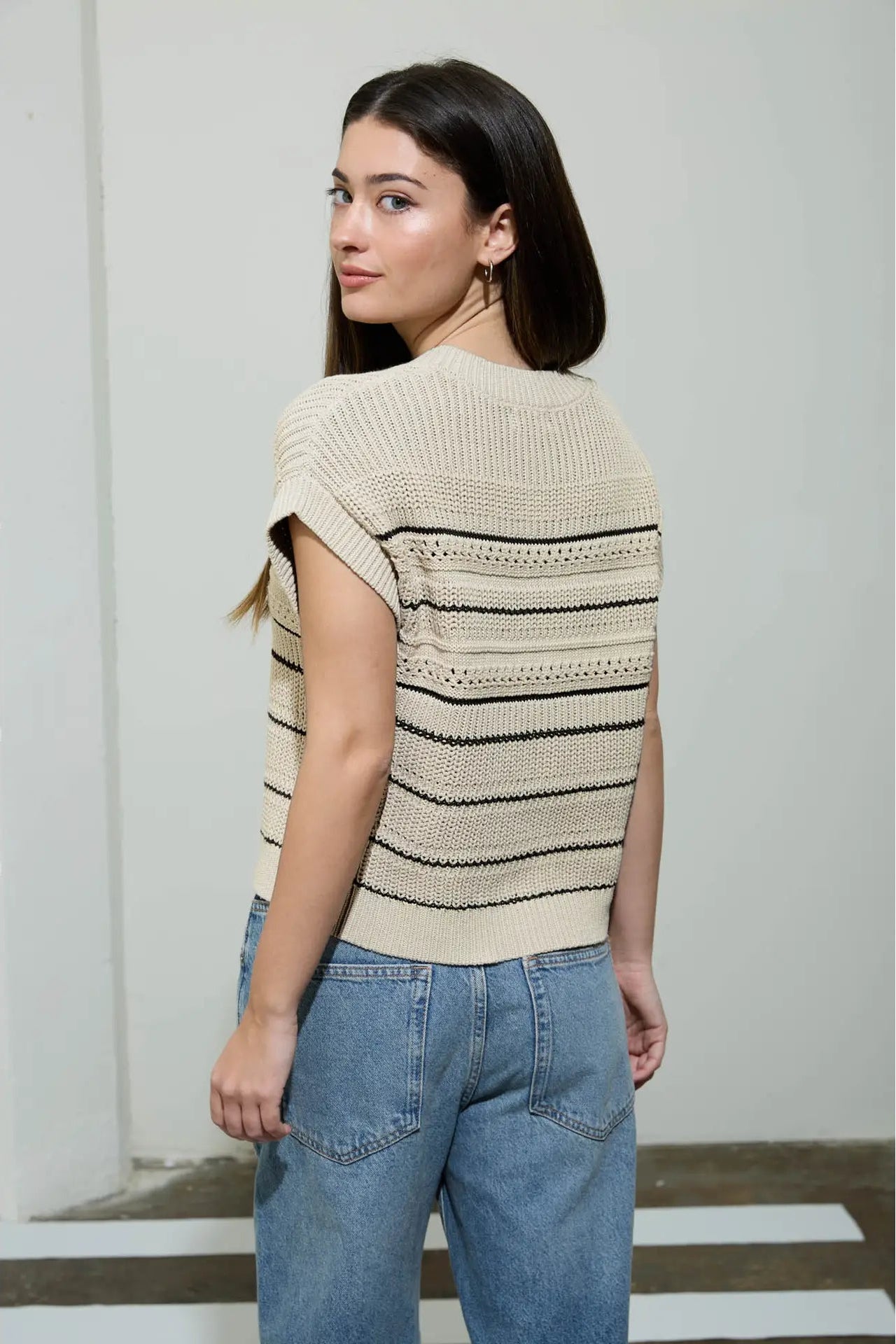 Woman wearing a beige and black striped sweater with blue jeans against a plain background