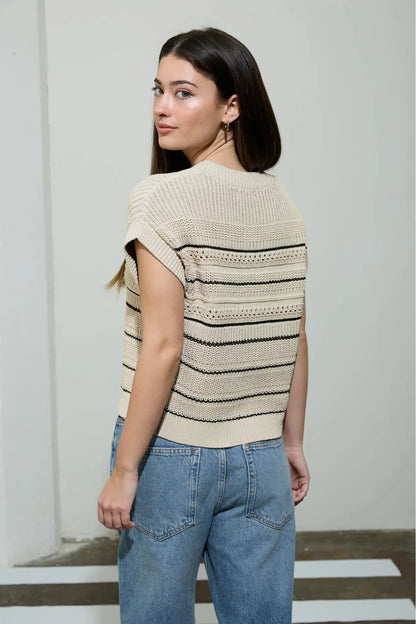 Woman wearing a beige and black striped sweater with blue jeans against a plain background