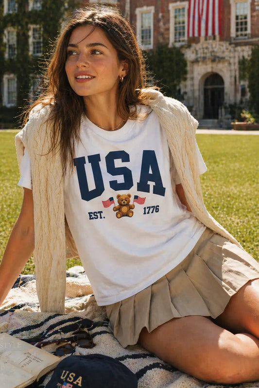Woman sitting on a blanket outdoors wearing a 'USA' t-shirt with a building in the background