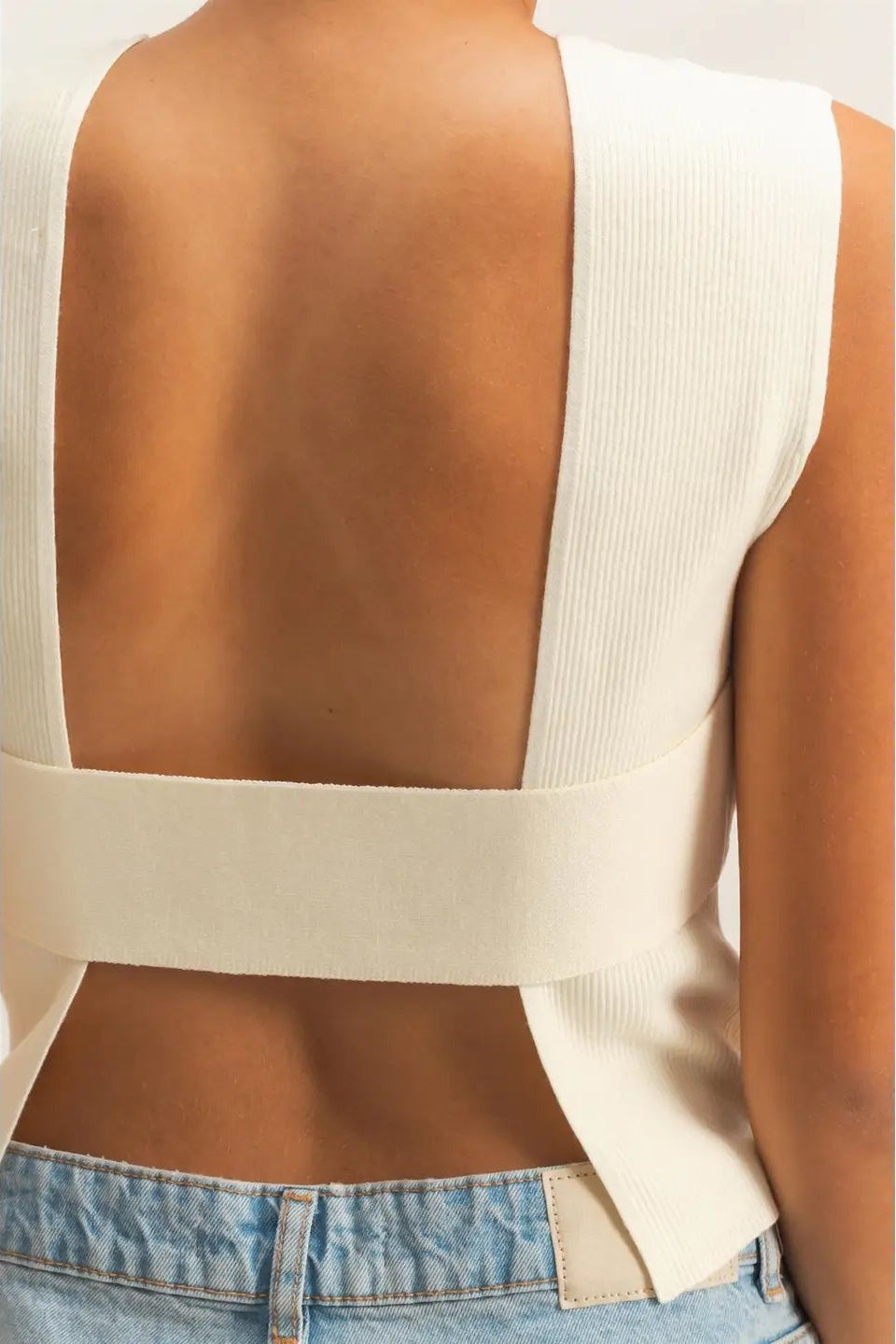 Beige sleeveless top with open back worn by a person on a white background