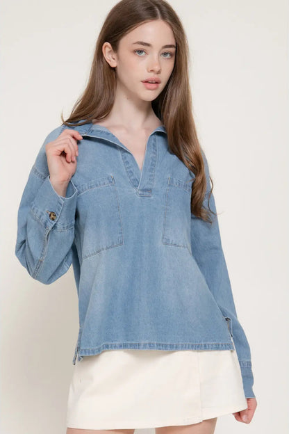 A woman wearing a light blue denim long-sleeve shirt with a split collar and a white skirt, photographed against a plain light beige studio background.