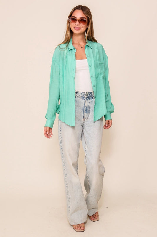 Woman wearing a light green shirt, white top, and light blue jeans against a beige background