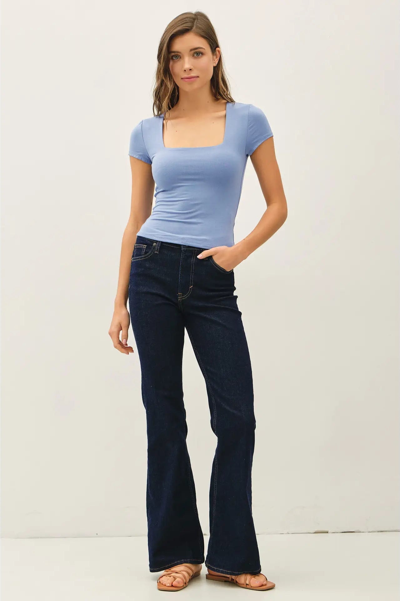 Woman wearing a blue top and dark blue jeans against a white background