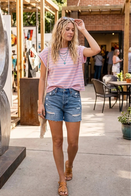 Woman wearing a striped pink and white t-shirt and denim shorts outdoors.