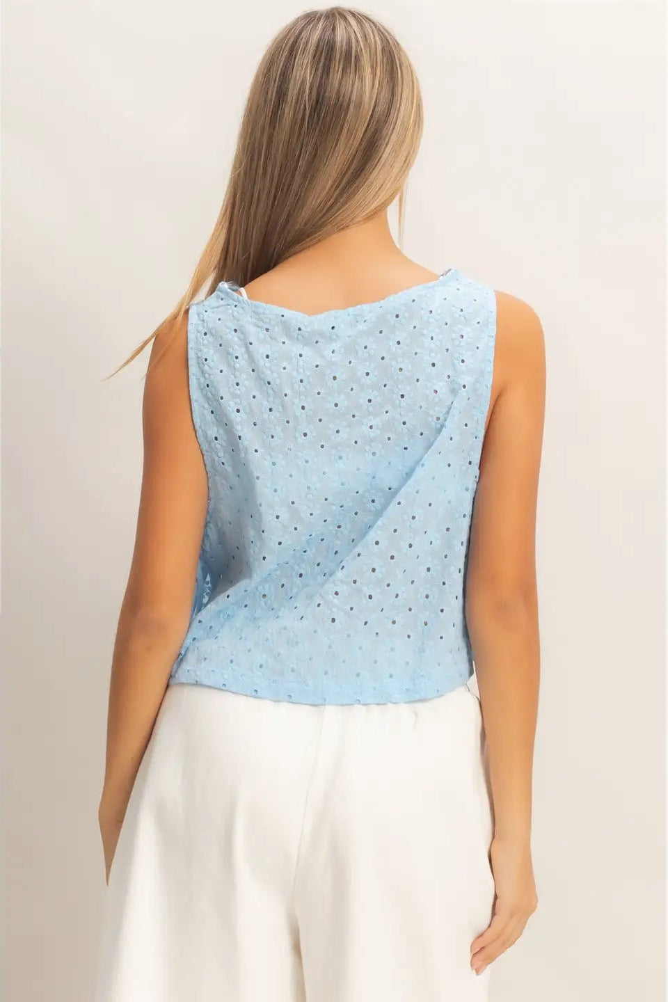Woman wearing a light blue sleeveless top with a geometric pattern on a plain background