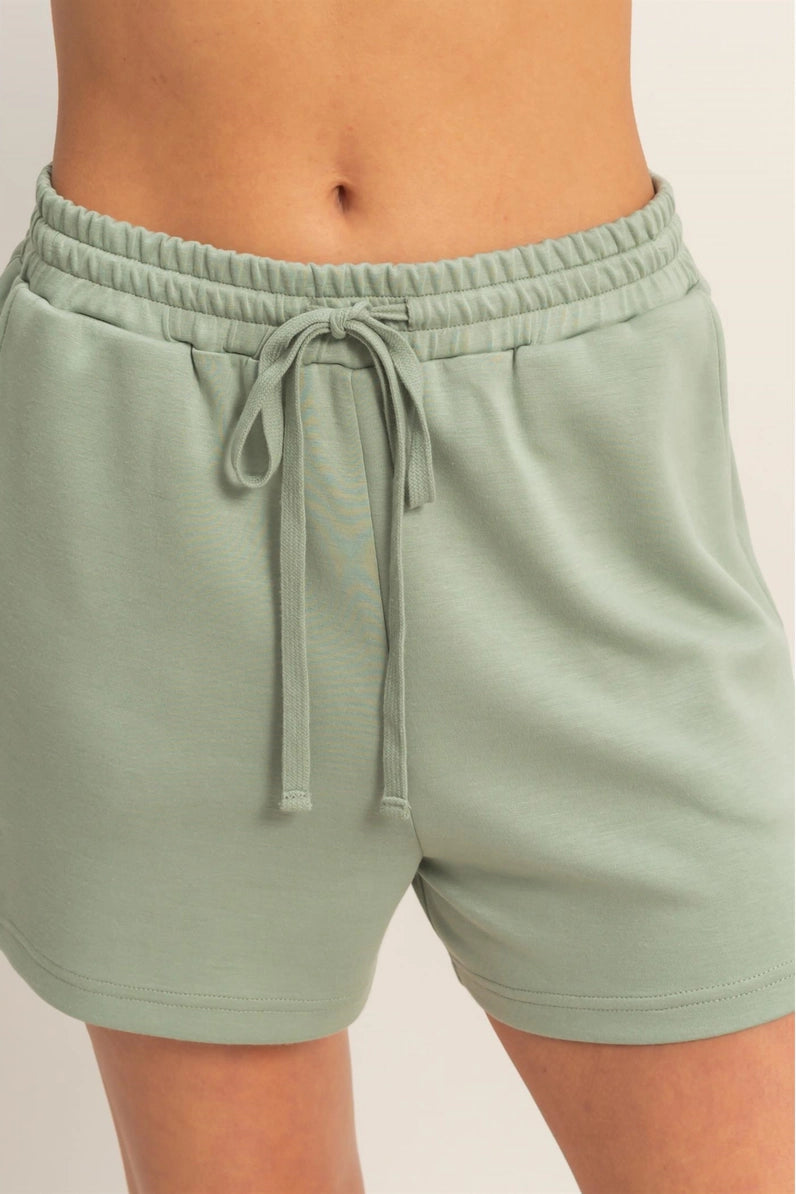 Sage green shorts with a drawstring on a plain background