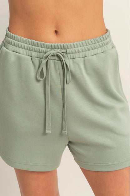 Sage green shorts with a drawstring on a plain background