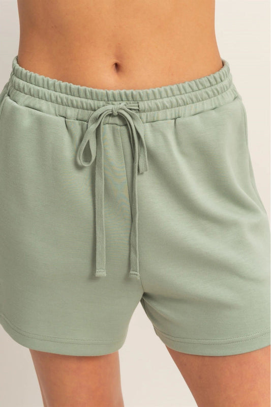 Sage green shorts with a drawstring on a plain background