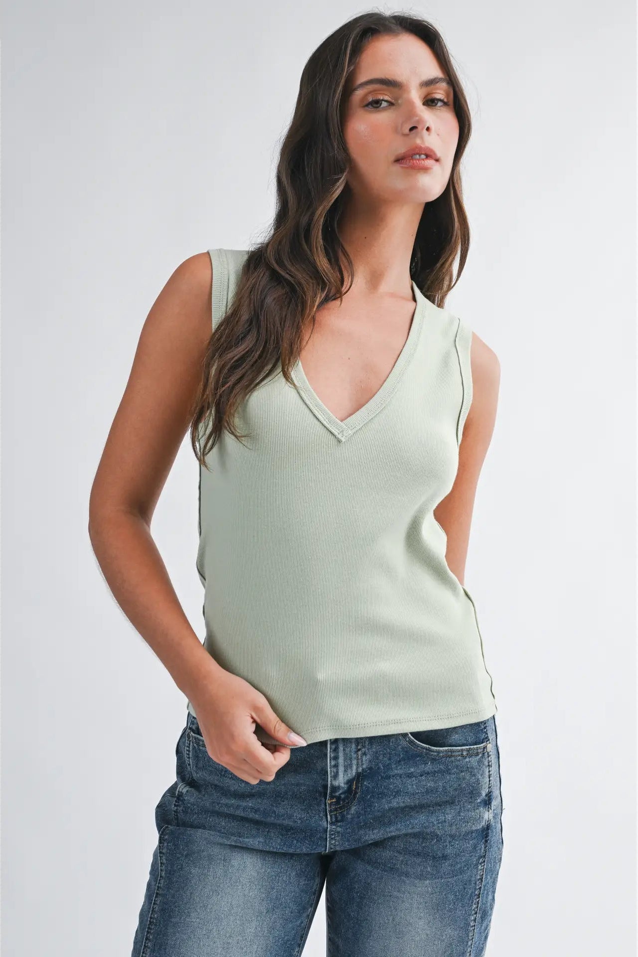 Woman wearing a light green sleeveless top and blue jeans on a white background