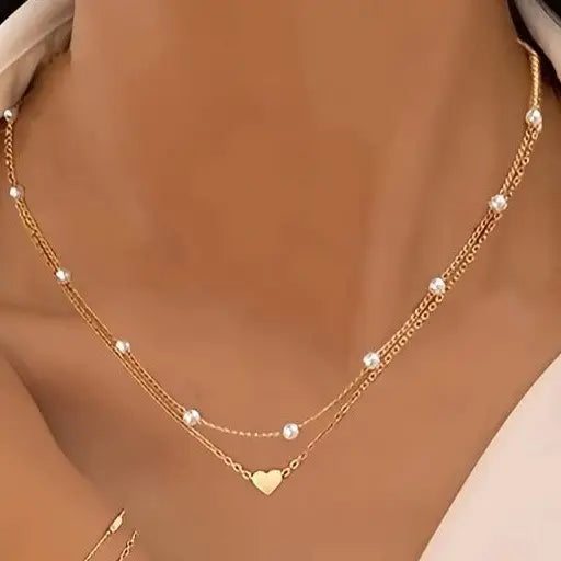 Gold necklace with heart pendant on a person wearing a beige top.